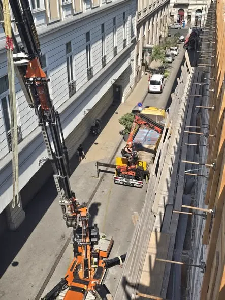 Autódaru gémje egy szűk belvárosi utca fölé fordulva, alatta lánctalpas emelőgép és teherautó a lezárt sávban, kétoldalt klasszikus bérházhomlokzatok