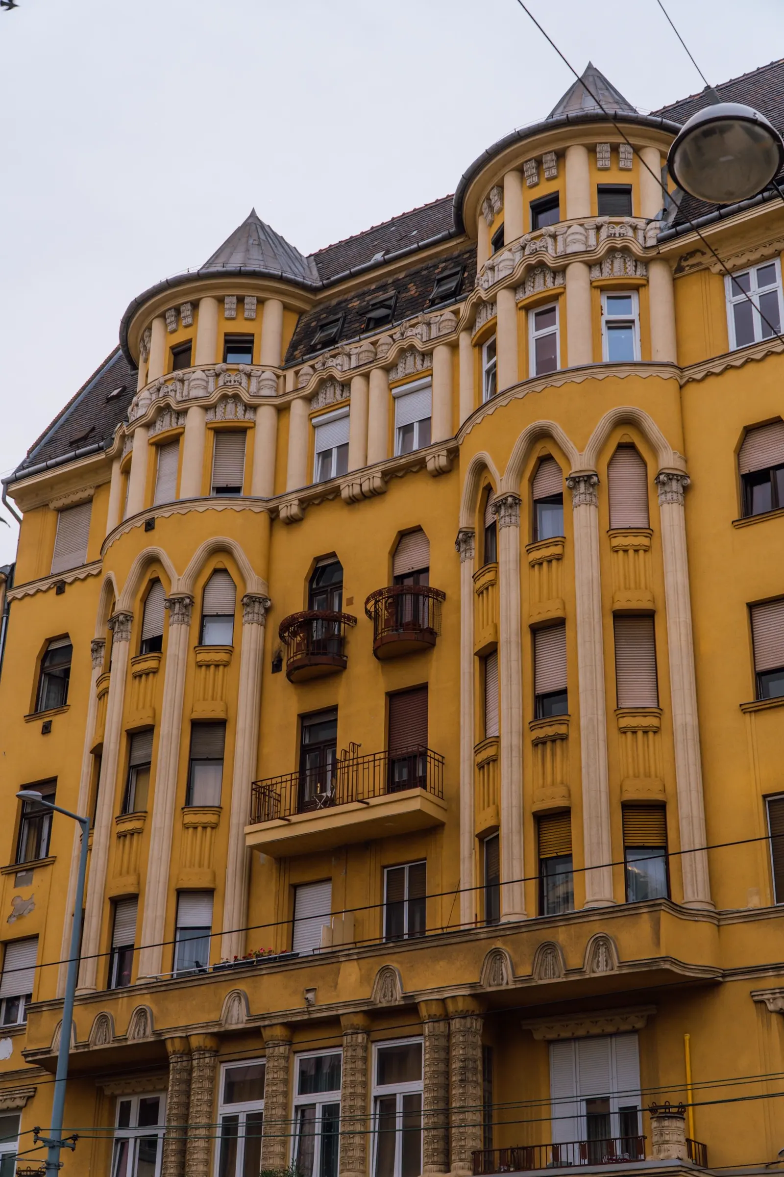 Szecessziós budapesti bérház sárga homlokzata, íves erkélyekkel és sarokerkélyes tornyokkal